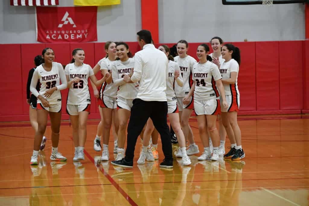 Albuquerque Academy girls' basketball team celebrating victory in gymnasium.