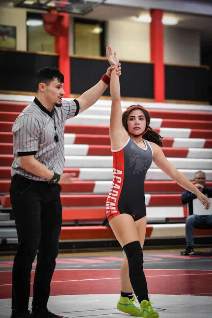 Albuquerque Academy student winning a wrestling match, referee raising her hand in victory.