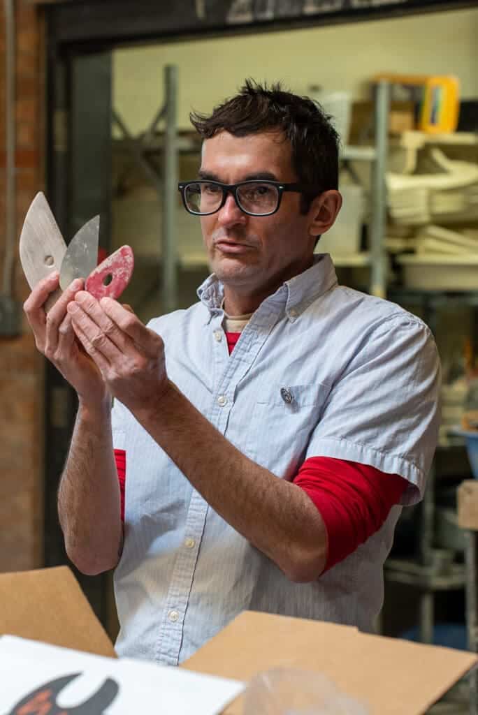 Handyman holding paint scrapers in workshop.