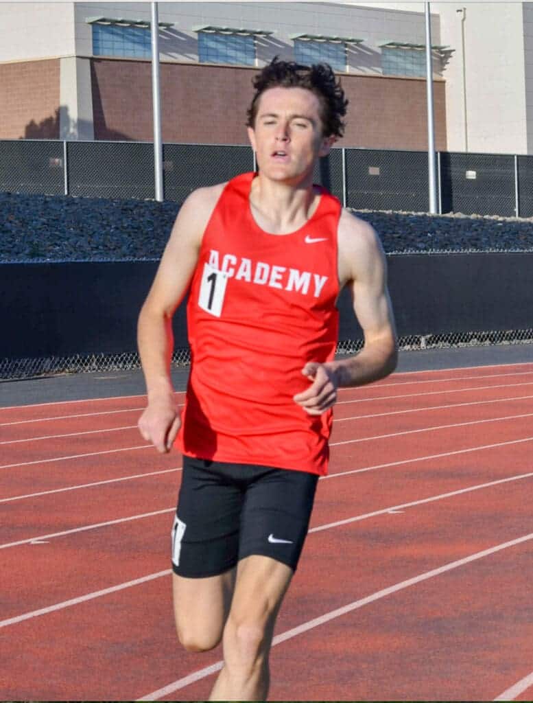 Albuquerque Academy student participating in track and field race at outdoor stadium.