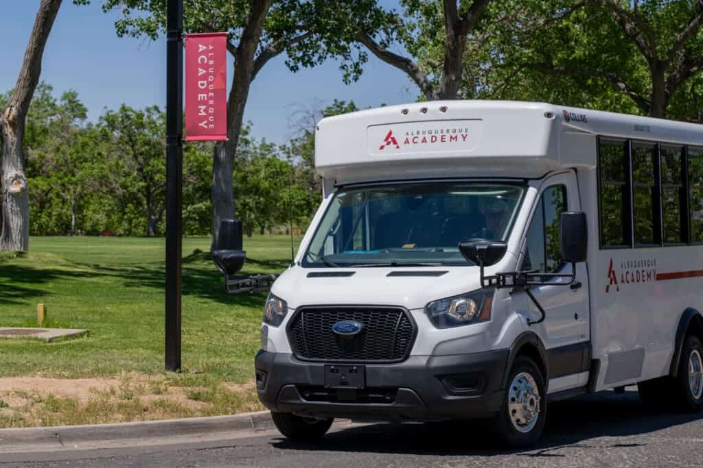 Albuquerque Academy shuttle bus parked on campus with school banner in background.