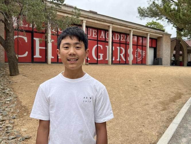 Albuquerque Academy student standing outside campus building with school sign in background.