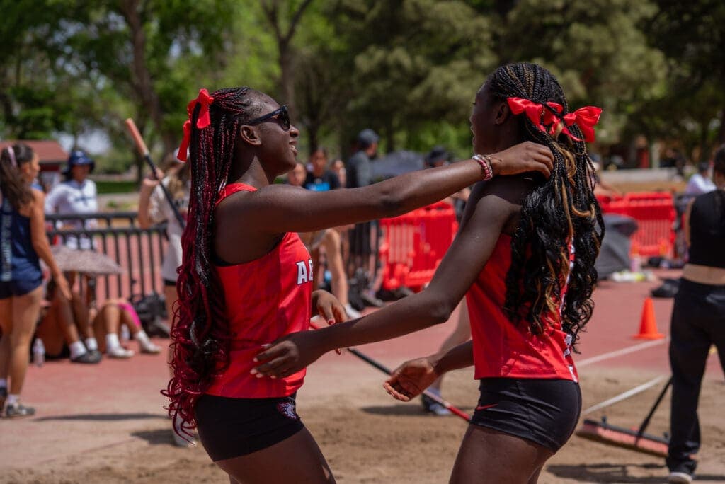 Albuquerque Academy students celebrating at track and field event in red athletic uniforms.