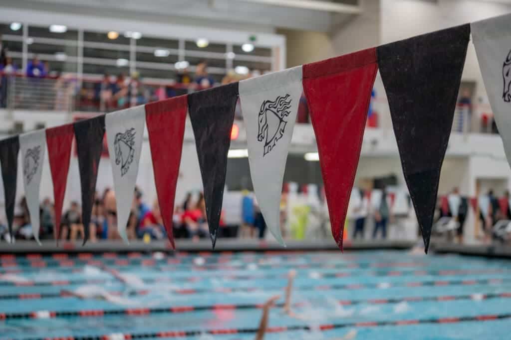 Albuquerque academy swim meet with red, black, and white pennant banners, athletes, and spectators.