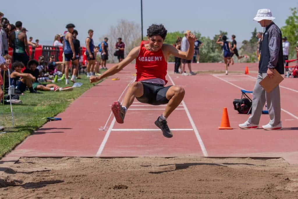Young male athlete in mid-air during long jump at Albuquerque Academy track and field meet.