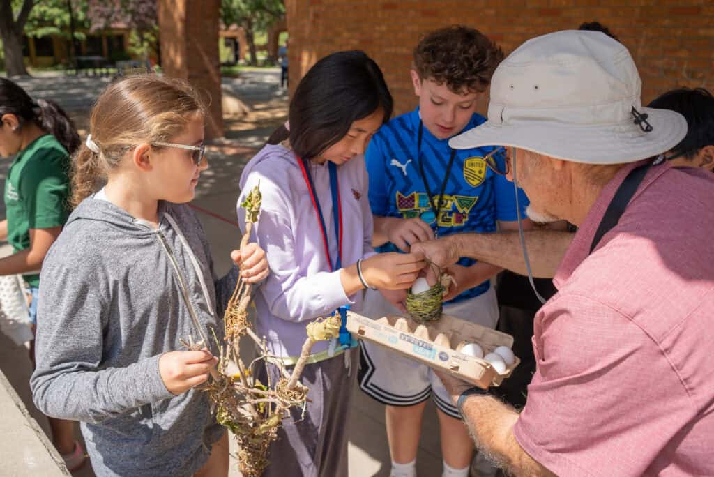 Handheld image of students at Albuquerque Academy participating in an outdoor educational activity, engaging with a teacher about eggs and bird nests, showcasing the school's focus on experiential learning and environmental education.