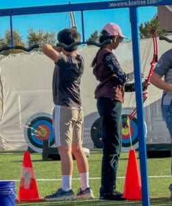 Albuquerque academy students practicing archery on athletic field during outdoor activities.
