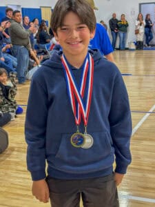 Medal-winning student at Albuquerque Academy school event, smiling with medals, indoor gym setting, student achievement celebration.