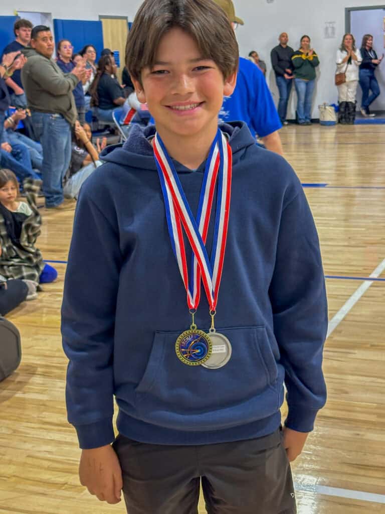 Medal-winning student at Albuquerque Academy school event, smiling with medals, indoor gym setting, student achievement celebration.