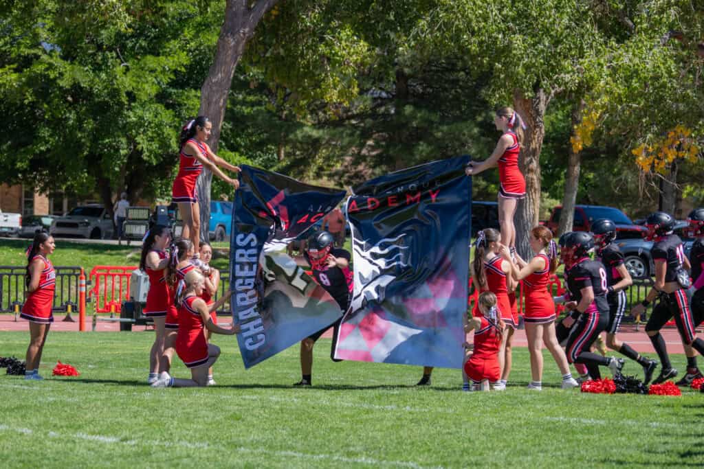 Albuquerque Academy cheerleaders holding a school banner during a game or event on campus.