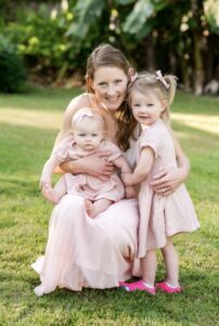 Smiling woman with two young daughters outdoors on green grass at Albuquerque Academy.