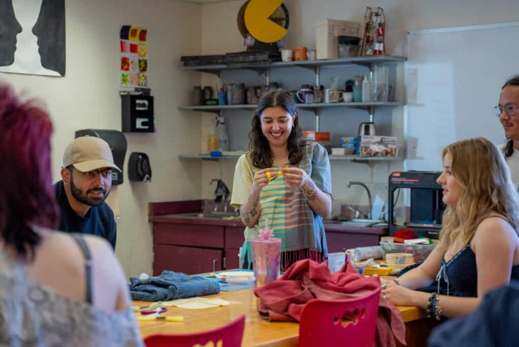 A woman demonstrating textile art to a group in an art classroom setting.