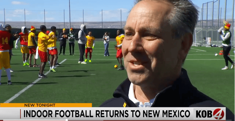 Indoor football practice at Albuquerque Academy with students and coaches on the field.
