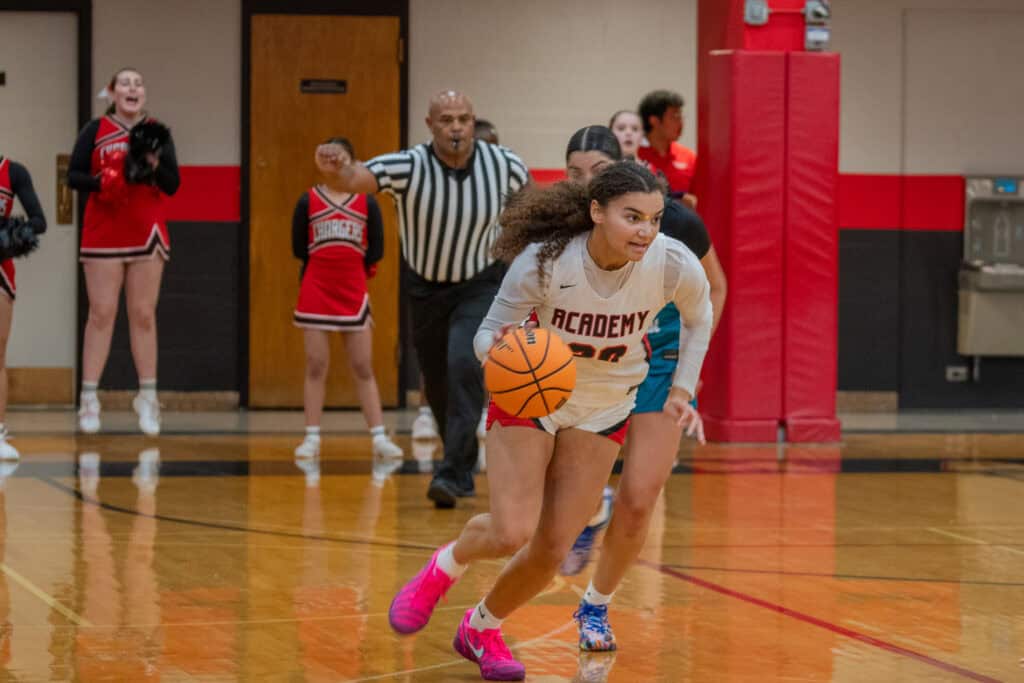 Albuquerque Academy student dribbling basketball during winter sports event at school gym.