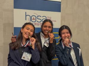 Three students smiling with medals at HOSA event