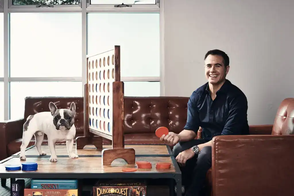 A man playing Connect Four with a French Bulldog in a modern lounge area at Albuquerque Academy.
