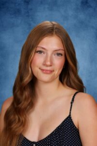 Albuquerque Academy student with long wavy hair smiling against blue background.