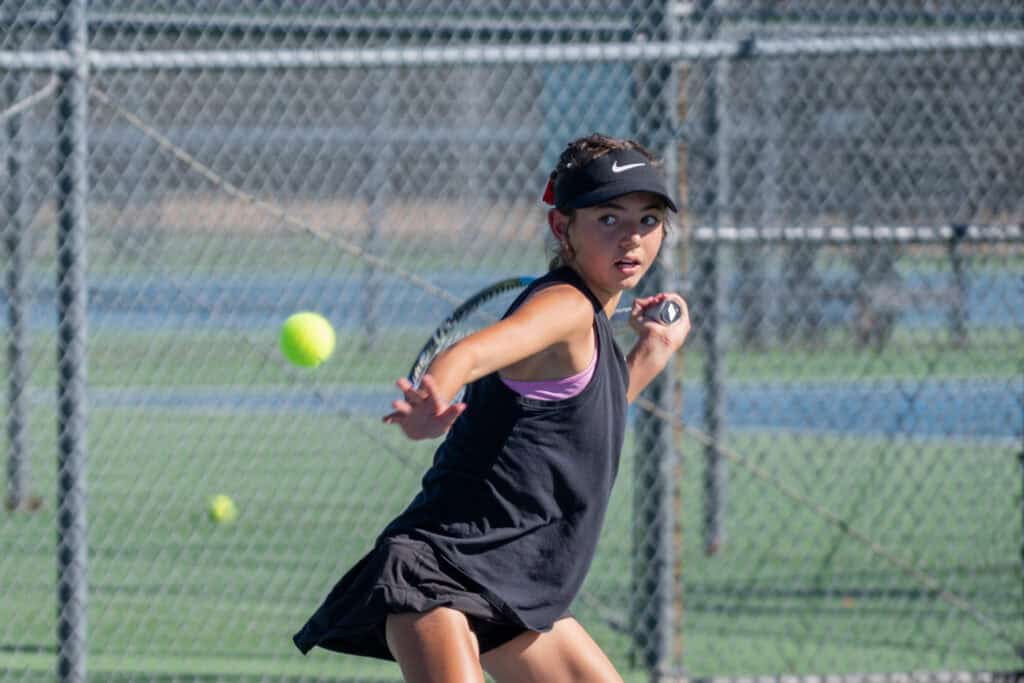 Albuquerque Academy girl tennis player hitting a ball during match on outdoor court.