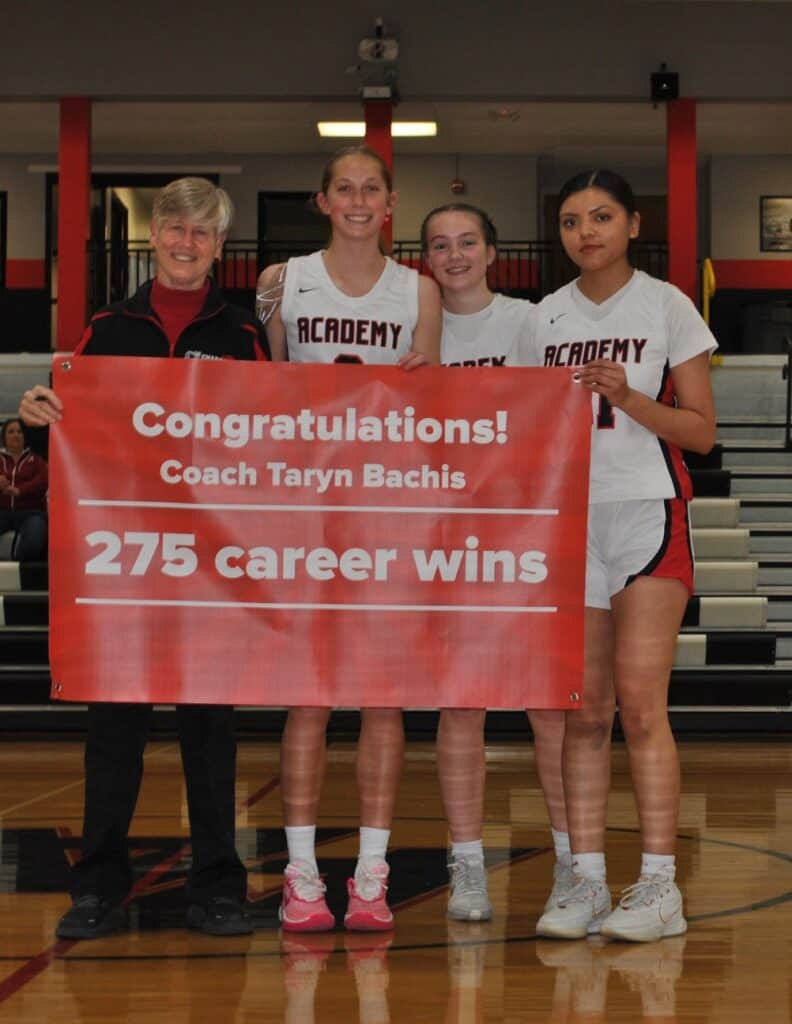 Celebrating Albuquerque Academy girls' basketball team with coach Taryn Bachis and a victory banner.