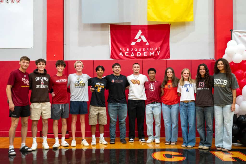 Albuquerque Academy students standing together in gymnasium with school banner and balloons.