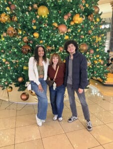 Three people posing before giant Christmas tree