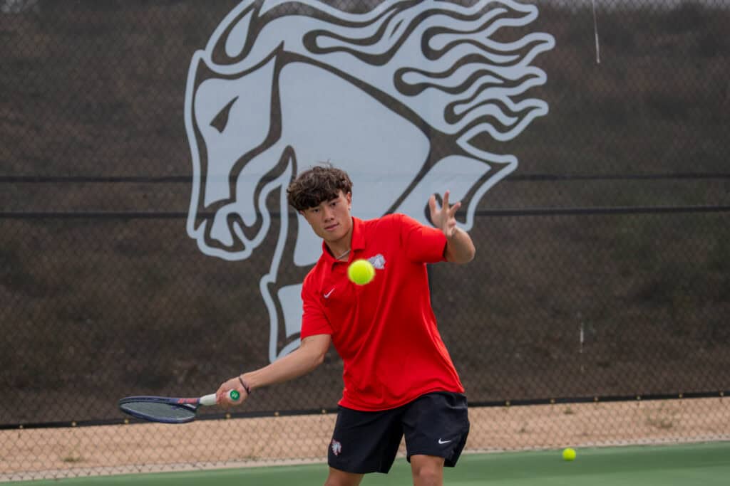Albuquerque Academy student playing tennis on school court with school logo in background.