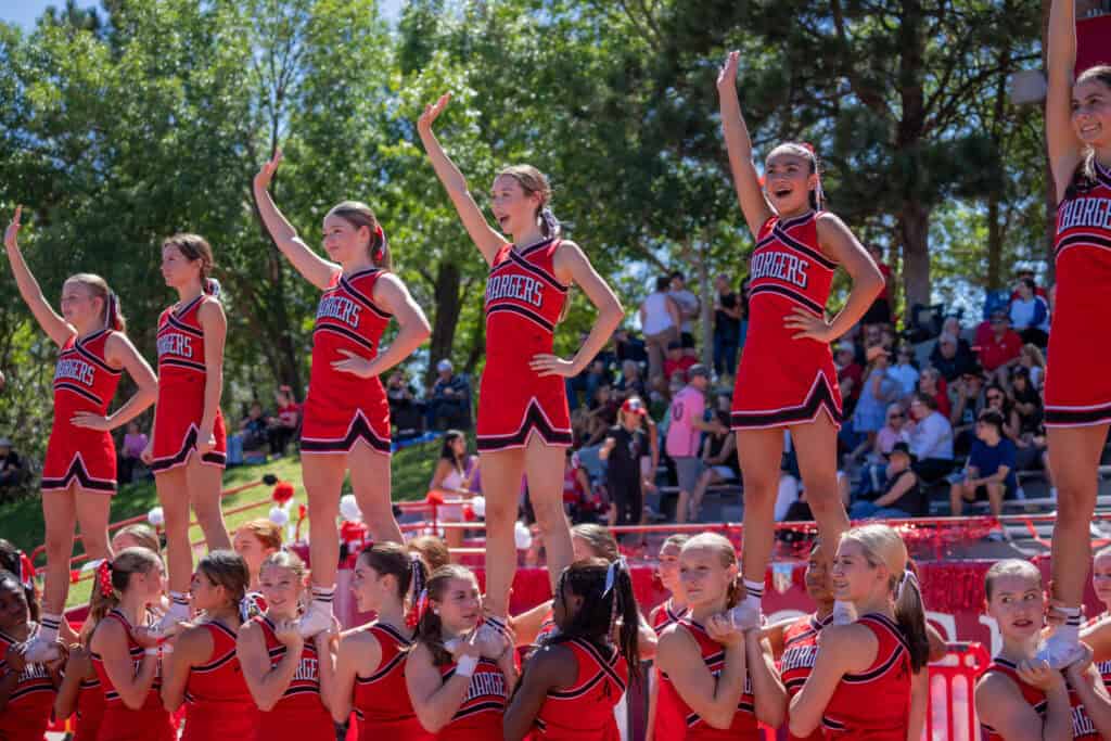 Albuquerque Academy cheerleaders performing at an outdoor event with spectators in the background.