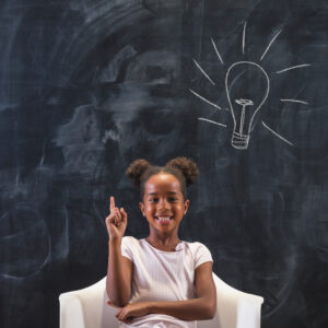 Smiling girl pointing at chalkboard light bulb drawing