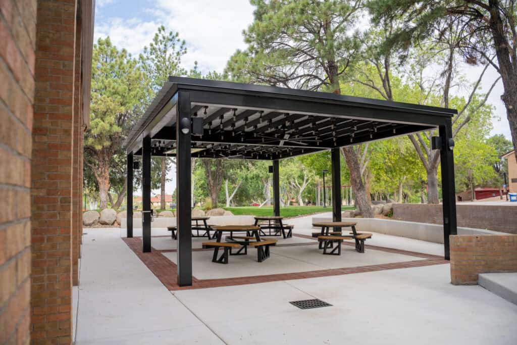 Albuquerque Academy outdoor covered picnic area with benches and trees in background.
