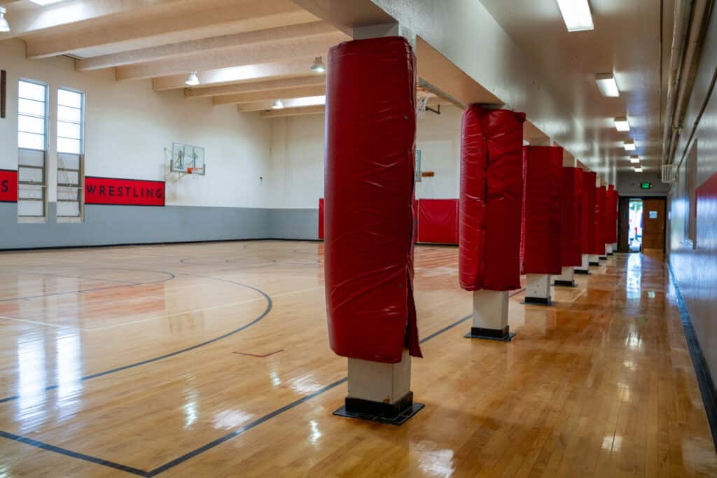 Albuquerque Academy gymnasium with red protective padding on poles and wrestling area.