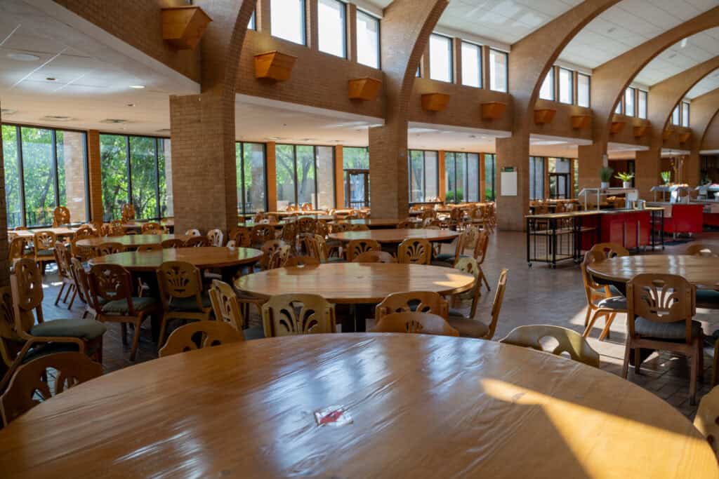 Interior of Albuquerque Academy cafeteria with wooden tables and large windows.
