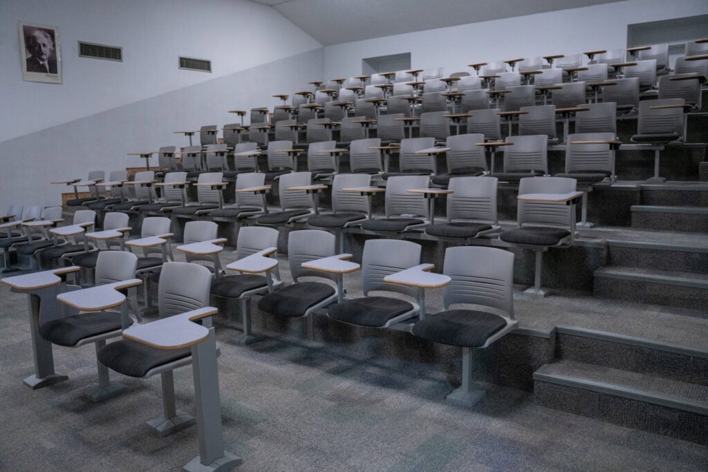Empty university lecture hall with tiered seating and desks.