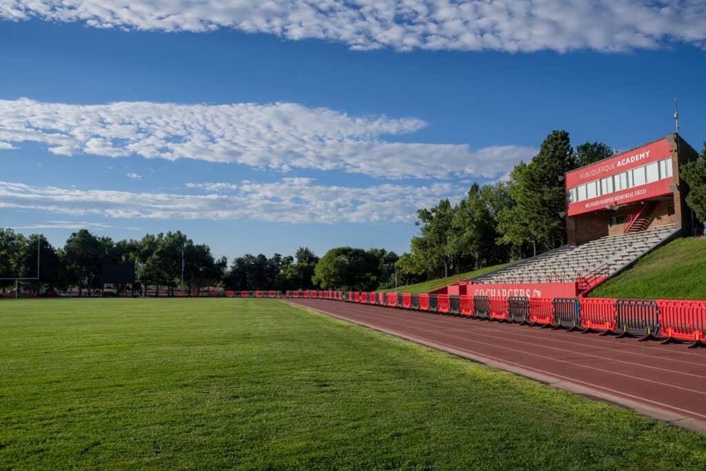 Albuquerque Academy sports field with track and bleachers under a blue sky.