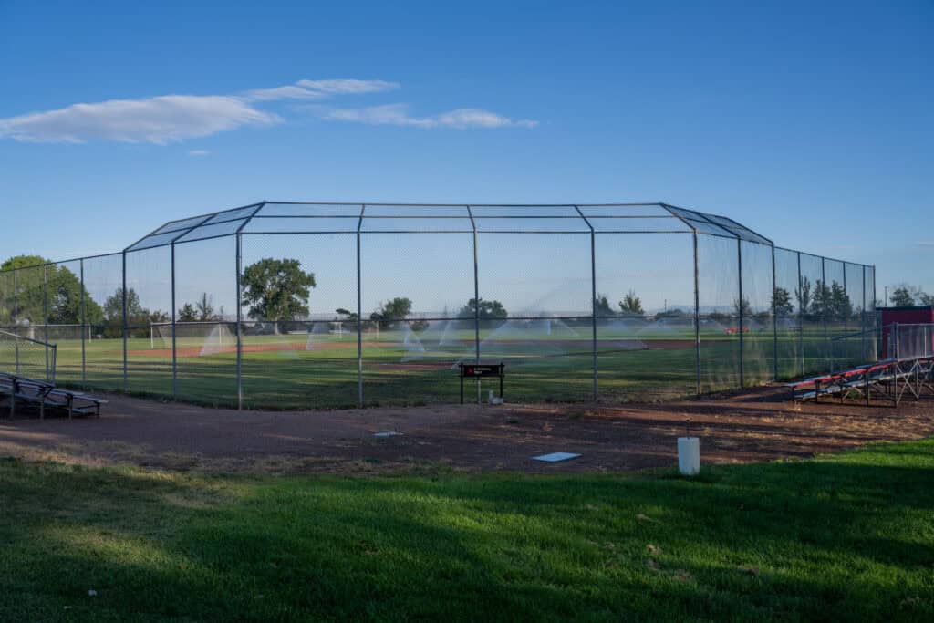 Albuquerque Academy baseball field with protective fencing and sprinklers in the background.
