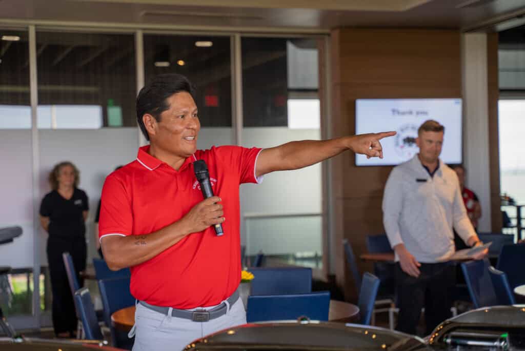 Man in red polo speaking and pointing at event in indoor setting.