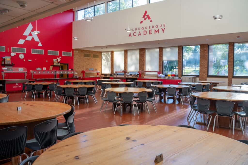Interior of Albuquerque Academy cafeteria with round tables and large windows.