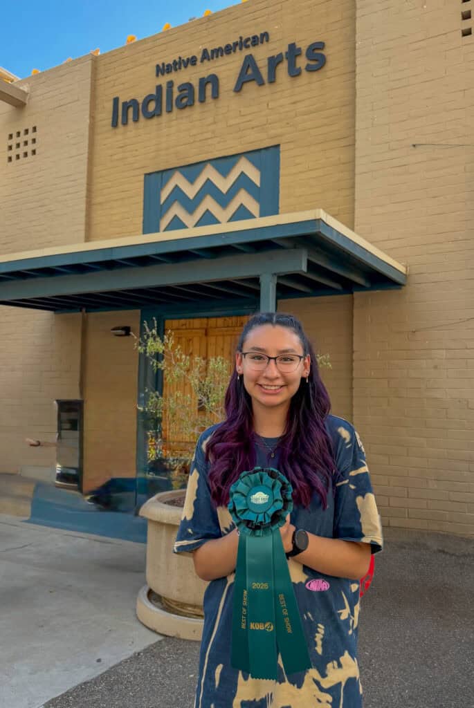 Young girl holding a blue ribbon in front of Albuquerque Academy Indian Arts building.