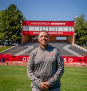 Albuquerque Academy coach standing on the field with stadium in background.