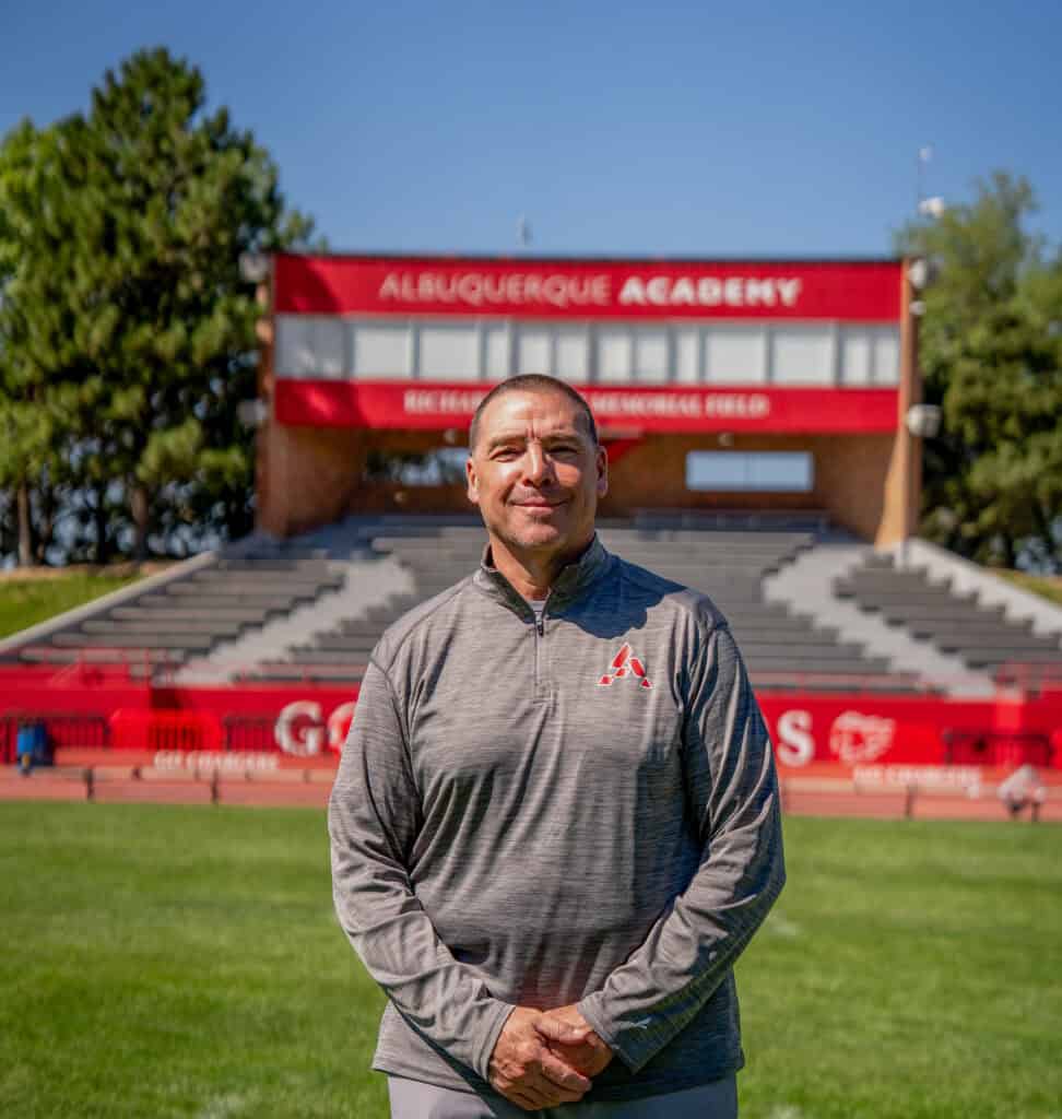 Albuquerque Academy coach standing on the field with stadium in background.