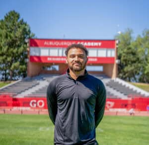 Young man standing on Albuquerque Academy football field with stadium in background.