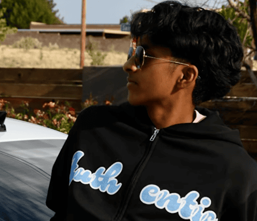 Young man wearing sunglasses and a black hoodie with 'truth' text outdoors.