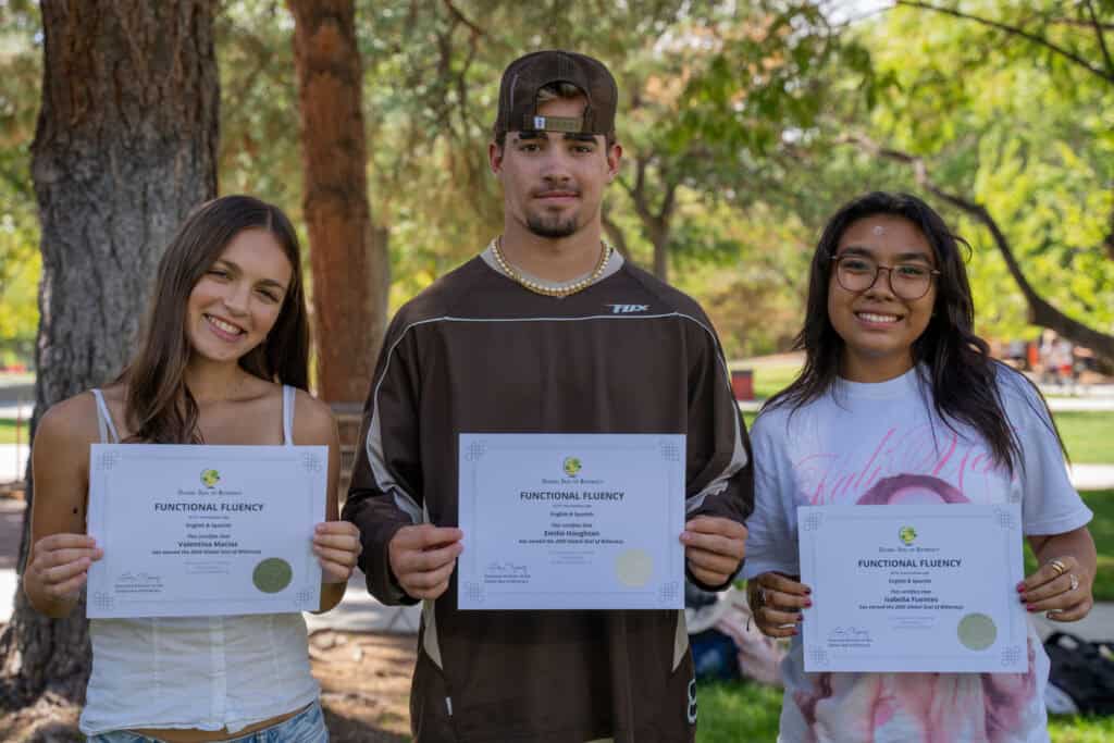 Three students holding certificates outdoors at Albuquerque Academy.