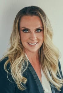 Portrait of a smiling woman with long blonde hair and blue eyes in professional attire.