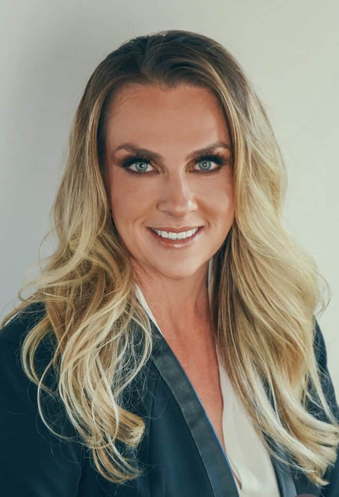 Portrait of a smiling woman with long blonde hair and blue eyes in professional attire.