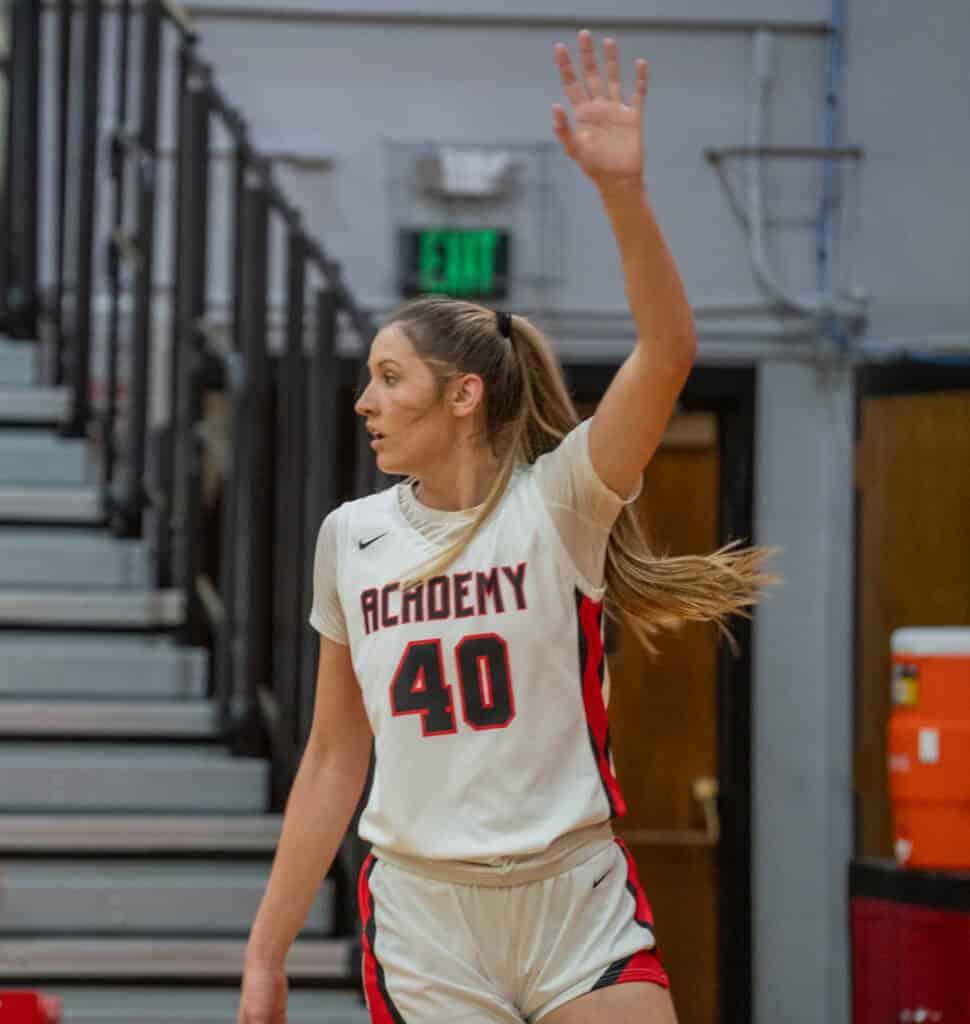 Female basketball player in white uniform with number 40 raises hand indoors.
